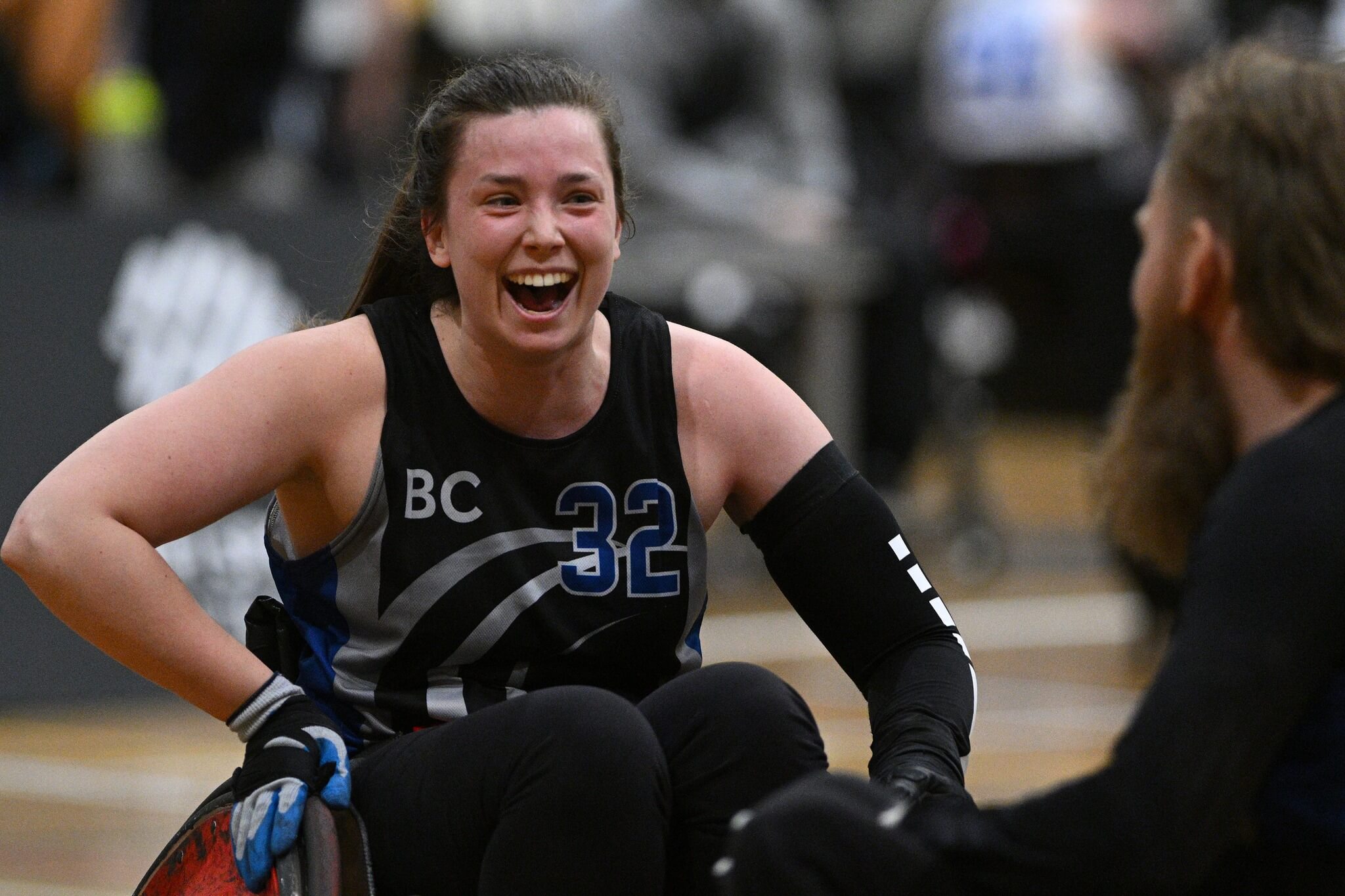 A woman smiles. She's in a rugby chair and wearing a black team bc jersey.