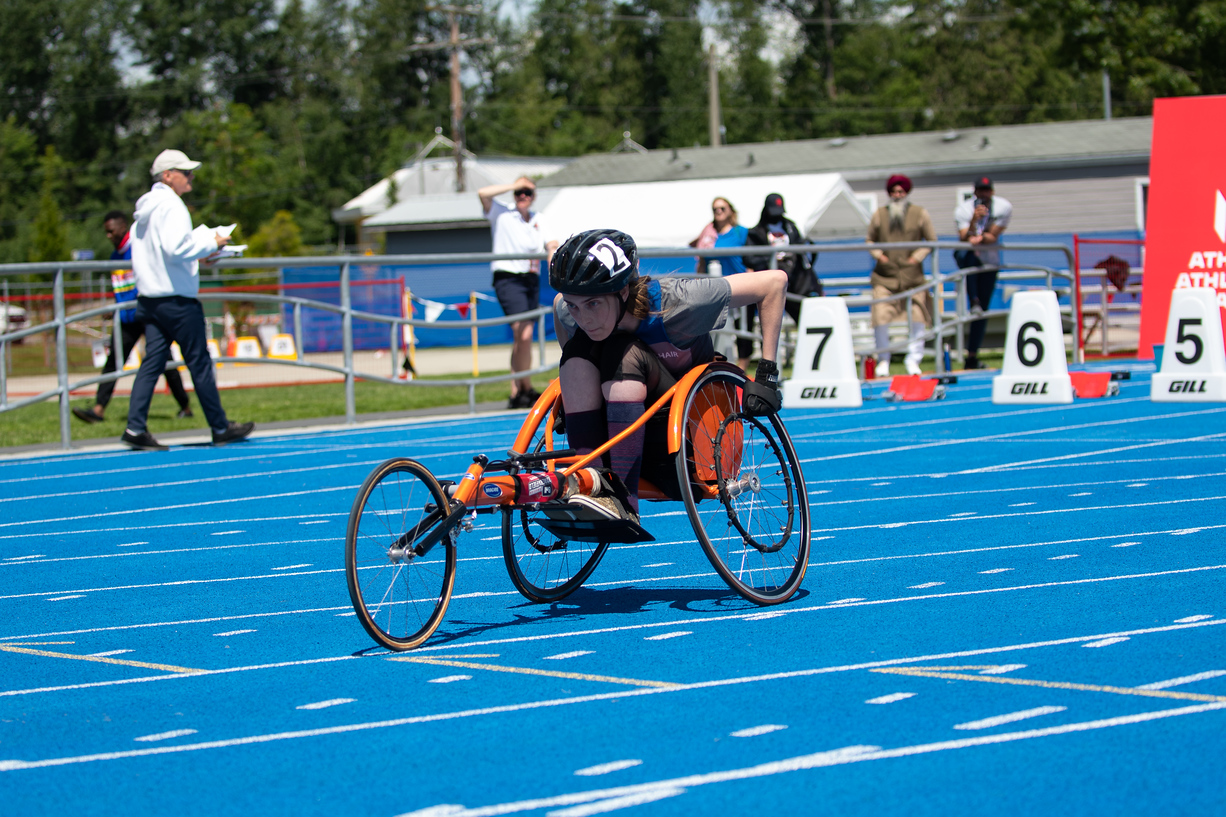 A woman in an orange racing chair pushes along the track.